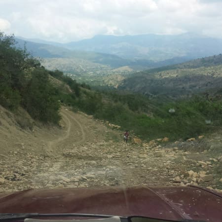 People living with poverty in Haiti driving down a dirt road with mountains in the background.