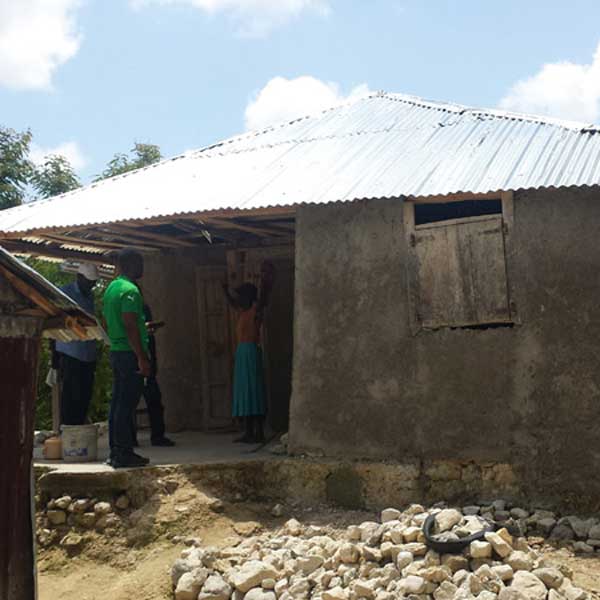 A group of people living with poverty in Haiti, standing in front of a house.