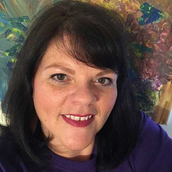 A woman in a purple shirt smiling in front of a painting, depicting resilience amidst poverty in Haiti.