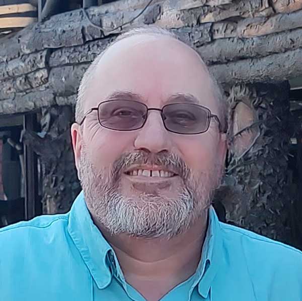 A man in a blue shirt smiles in front of a tree, representing people living with poverty in Haiti.
