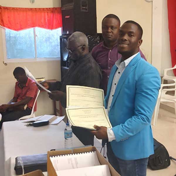 A man holding a certificate in front of a group of people living with poverty in Haiti.