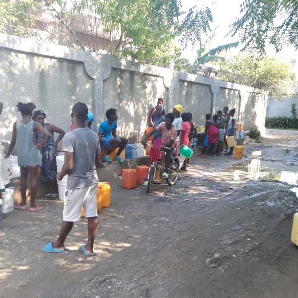 A group of people living with poverty in Haiti, standing outside with buckets of water.