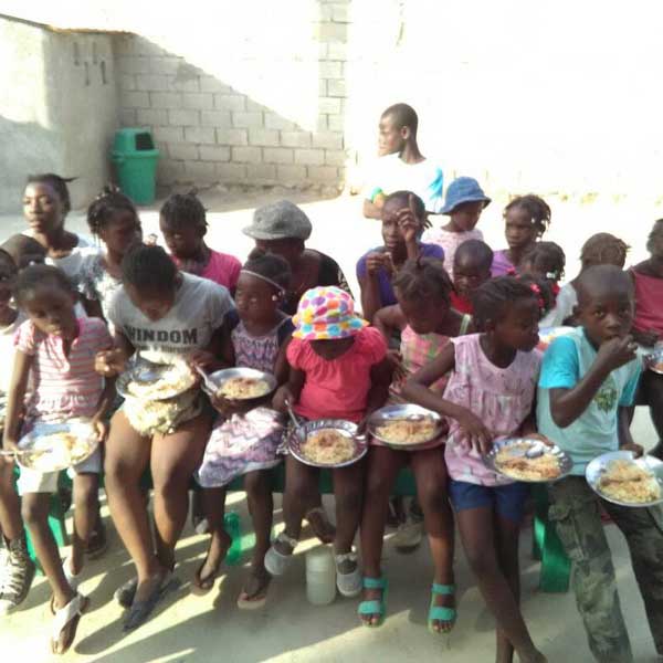 People living with poverty in Haiti, including a group of children sitting on the ground with plates of food.