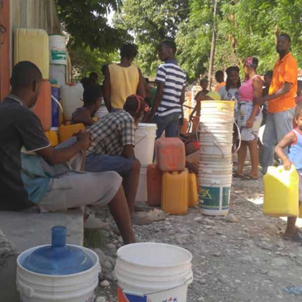 A group of people living with poverty in Haiti standing near buckets of water.